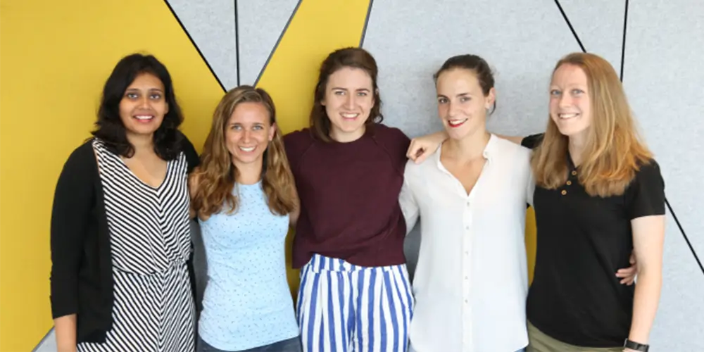 five women stand in front of geometric wall