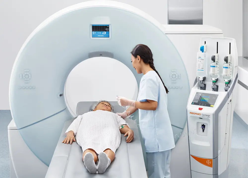 Clinican guides an elderly woman into a CT scanner with the Medrad Centargo Contrast injector to her right