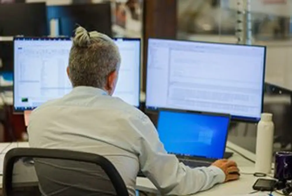 man views computer screen across 2 monitors in office