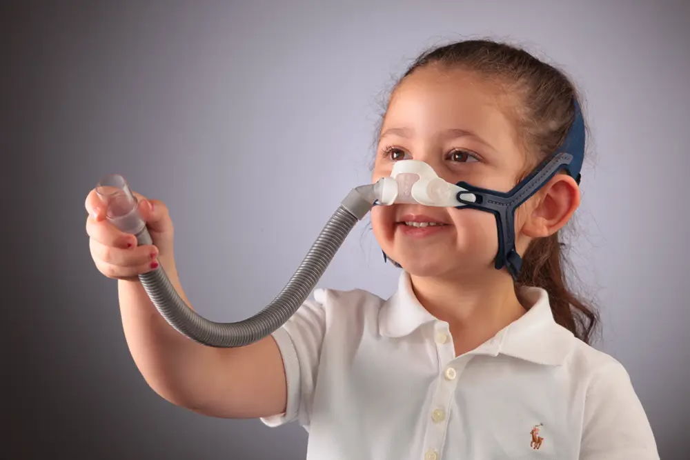 child wearing resmed pixi mask holds hose up to camera