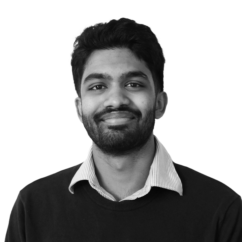 Black and white portrait of a man with a beard, smiling, wearing a collared shirt and sweater against a plain background.